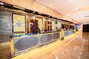 A reception area with a marble floor, a reception desk with a patterned design, and a wall with framed artwork. - Baiyun Hotel (West Building) (Lanzhou)