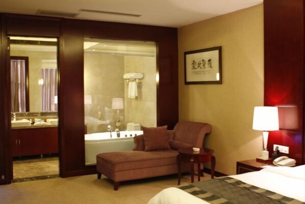 Ein Hotelzimmer mit Bett, Sessel, kleinem Tisch, Nachttisch, Lampe, Spiegel und einem Badezimmer mit Badewanne und Waschbecken.