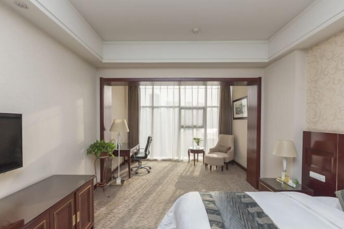 Ein Hotelzimmer mit einem Bett, einem Fernseher, einem Schreibtisch, einem Stuhl, einem kleinen Tisch und einem Fenster.
