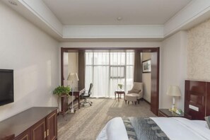 Ein Hotelzimmer mit einem Bett, einem Fernseher, einem Schreibtisch, einem Stuhl, einem kleinen Tisch und einem Fenster.