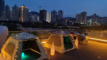 Une terrasse sur le toit, agrémentée de tentes, avec la silhouette de la ville en arrière-plan.
