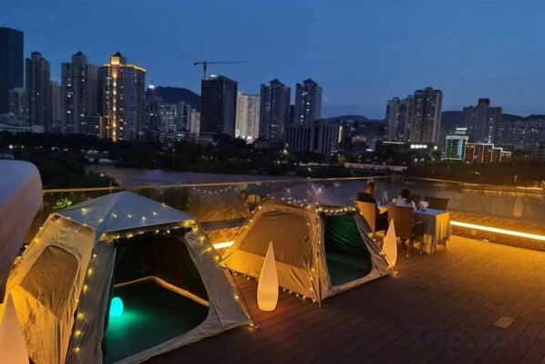 A rooftop terrace with tents and a city skyline in the background.