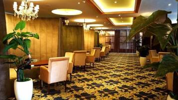 Vestíbulo de hotel con alfombra estampada, zona de estar y grandes macetas.