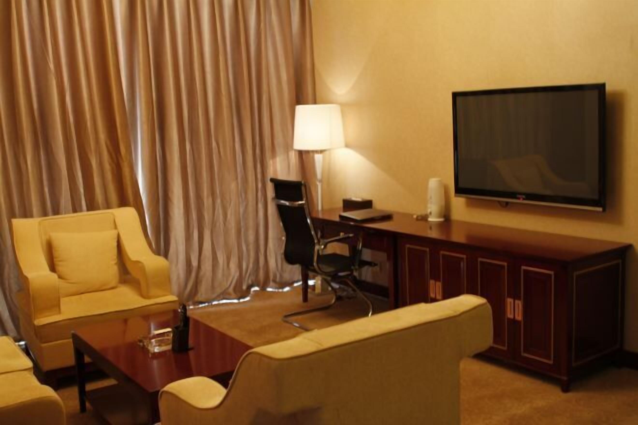 Ein Hotelzimmer mit einer Sitzecke, einem Schreibtisch, einem Sessel, einem Fernseher und einer Lampe.