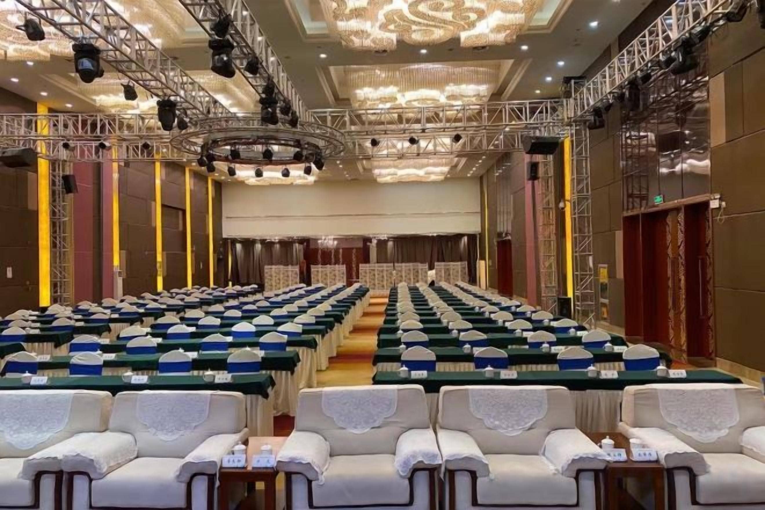 Un salón de conferencias amplio con filas de mesas y sillas, un escenario y un candelabro.