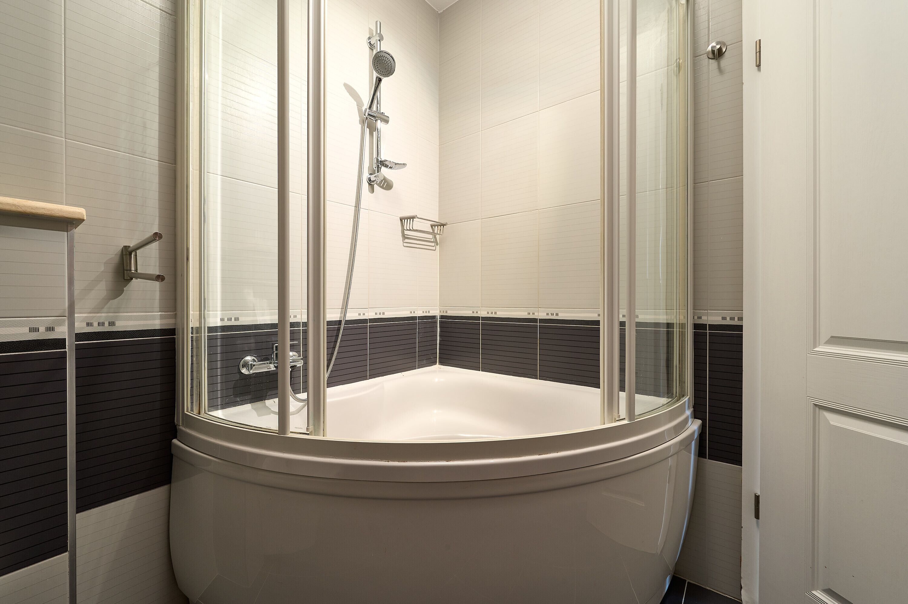 A modern bathroom with a freestanding bathtub, a glass-enclosed shower, and a black and white tiled wall.
