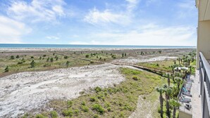 Un balcón con vistas a una playa y un paseo marítimo de madera.