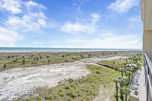 Un balcon avec vue sur une plage et une promenade en bois.