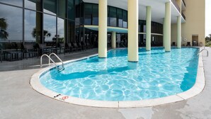 Zona de piscina con agua azul cristalina, una escalera de piscina y un área de descanso con sillas y mesas.