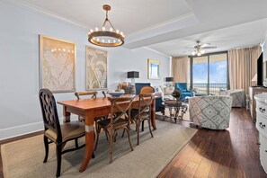 Un coin repas avec une table et des chaises en bois, un lustre, et un salon avec un canapé et un ventilateur de plafond.