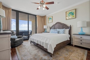 A bedroom with a large bed, a ceiling fan, a view to the outside, and a balcony.