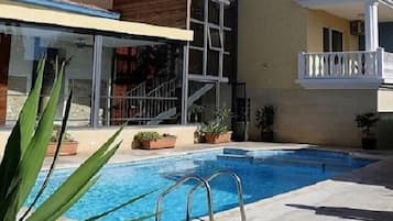 A swimming pool with a metal ladder, surrounded by potted plants and a building with balconies.