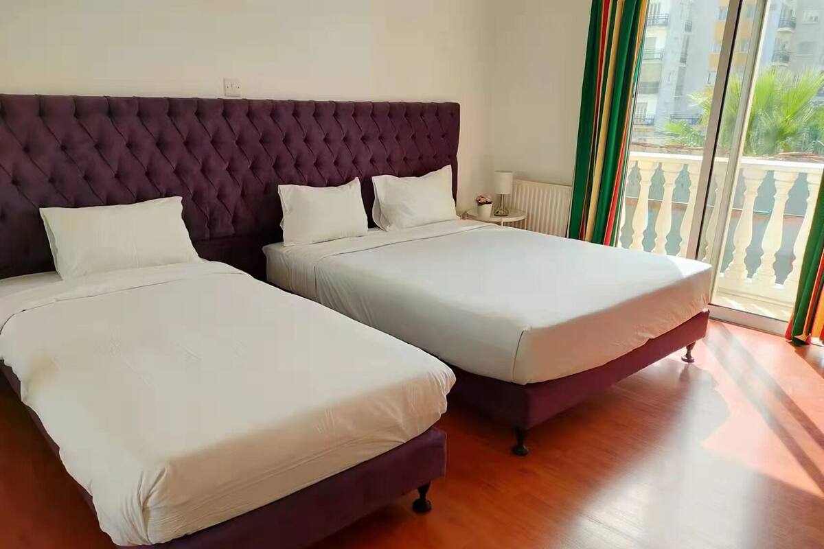 Habitación de hotel con dos camas, cabecera capitonada y balcón con vistas a la ciudad.