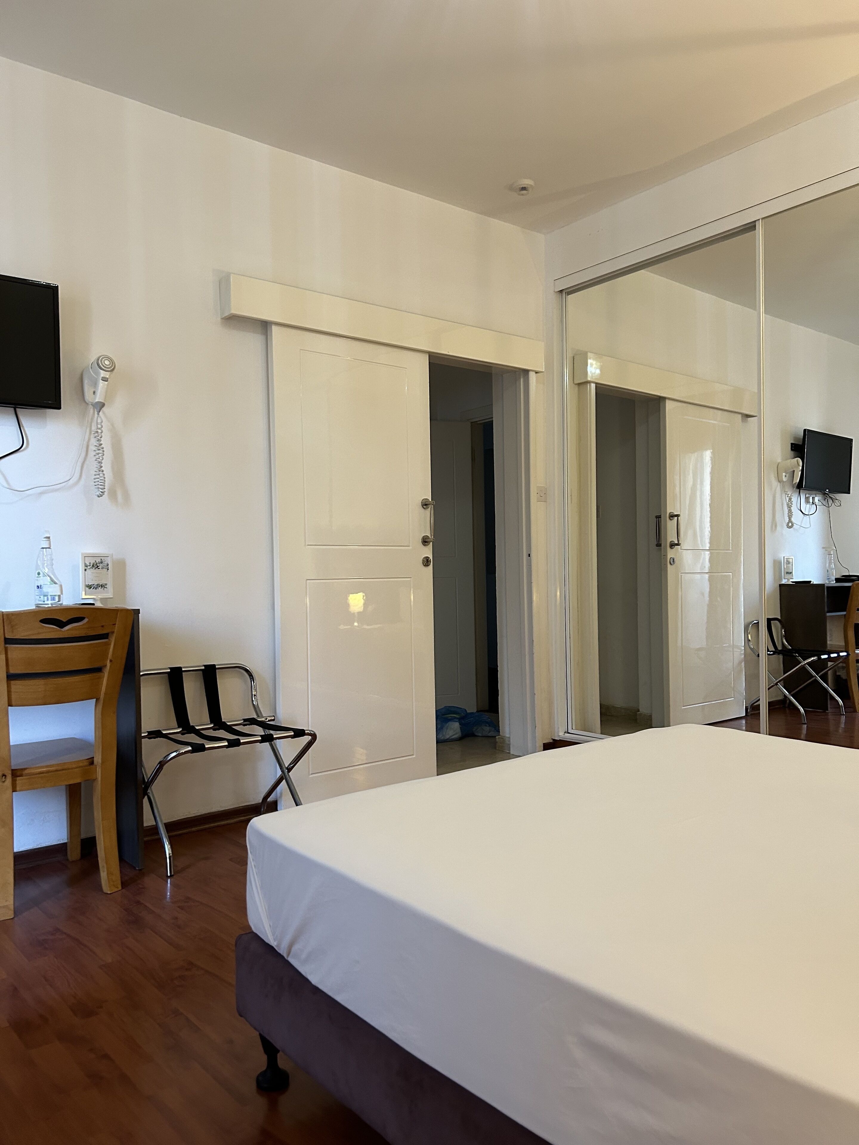 A bedroom with a bed, a desk, a chair, a television, and a door leading to another room.