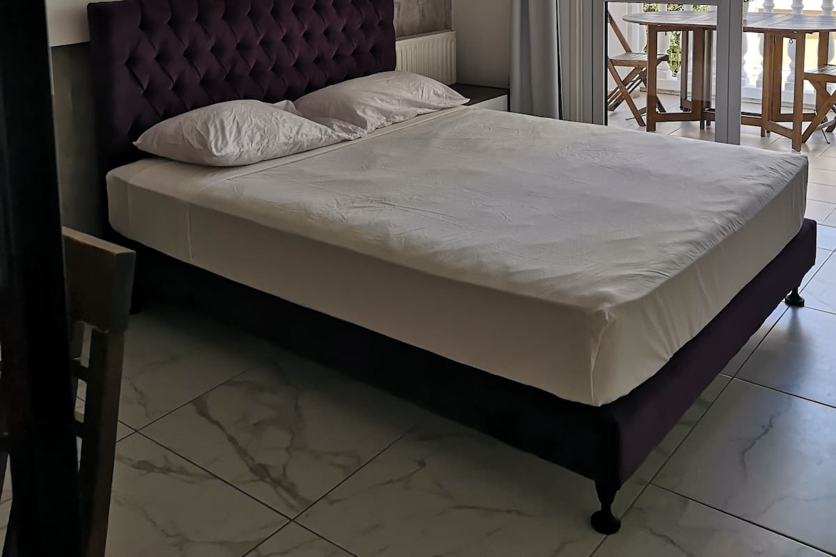 Una cama con cabecera capitonada, ropa de cama blanca y suelo con diseño de mármol.