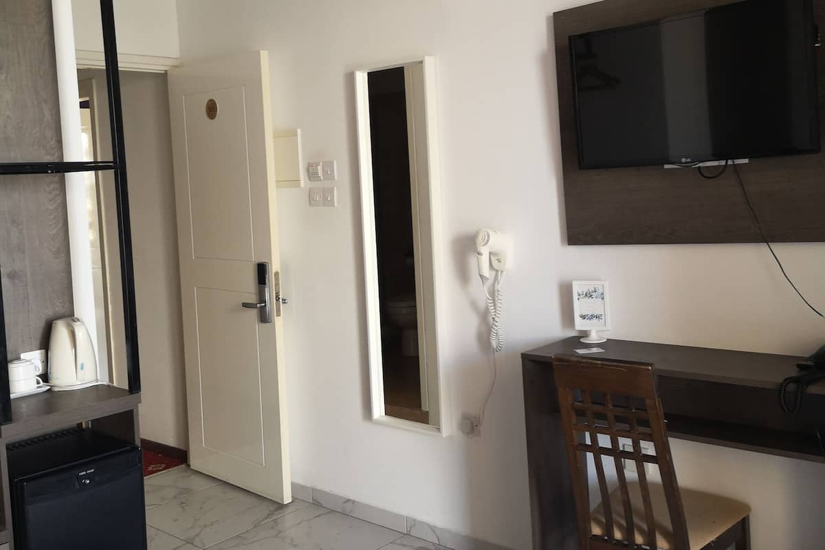Habitación de hotel con cama, escritorio con silla, televisor montado en la pared, secador de pelo y cafetera.