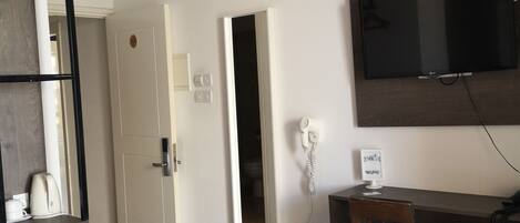 Habitación de hotel con cama, escritorio con silla, televisor montado en la pared, secador de pelo y cafetera.