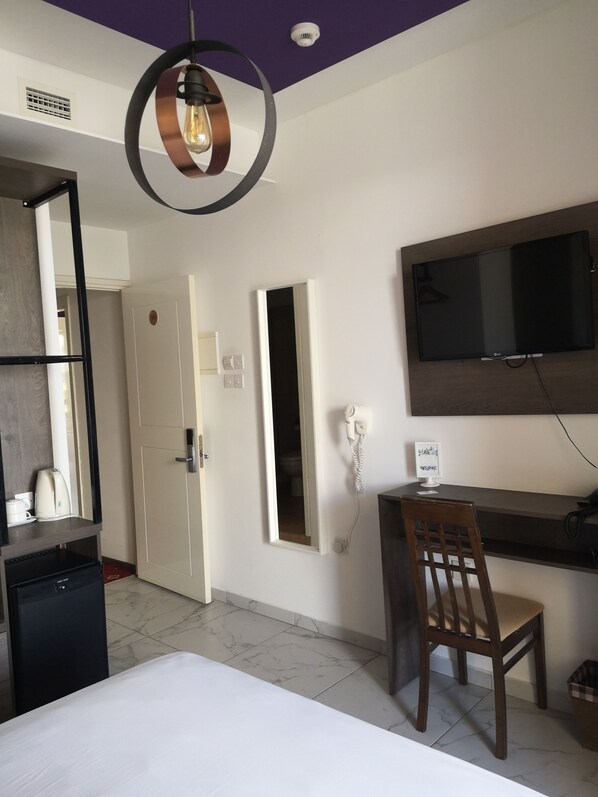 A hotel room with a bed, a desk with a chair, a television mounted on the wall, a hairdryer, and a coffee maker. - Elena Boutique Residence (Larnaca)