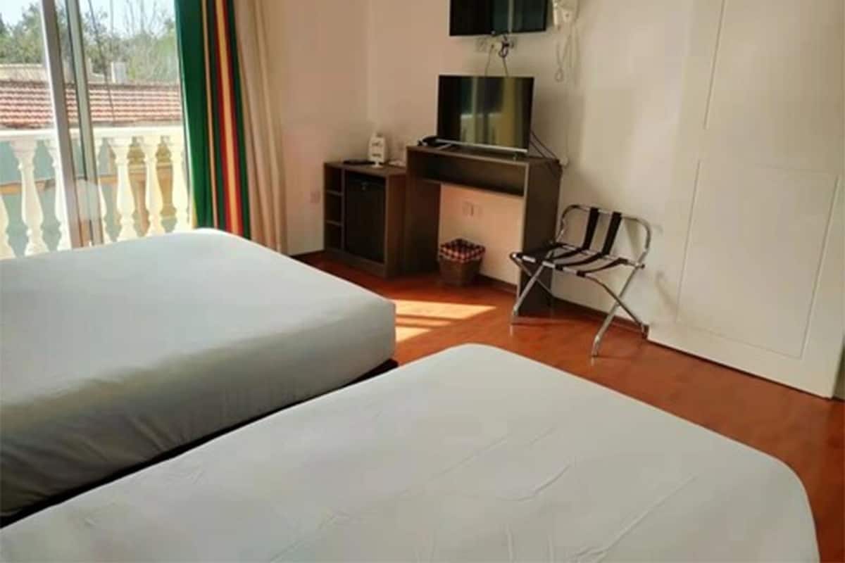 Una habitación con dos camas, un escritorio, una silla, un televisor y una ventana con vista a una cerca.