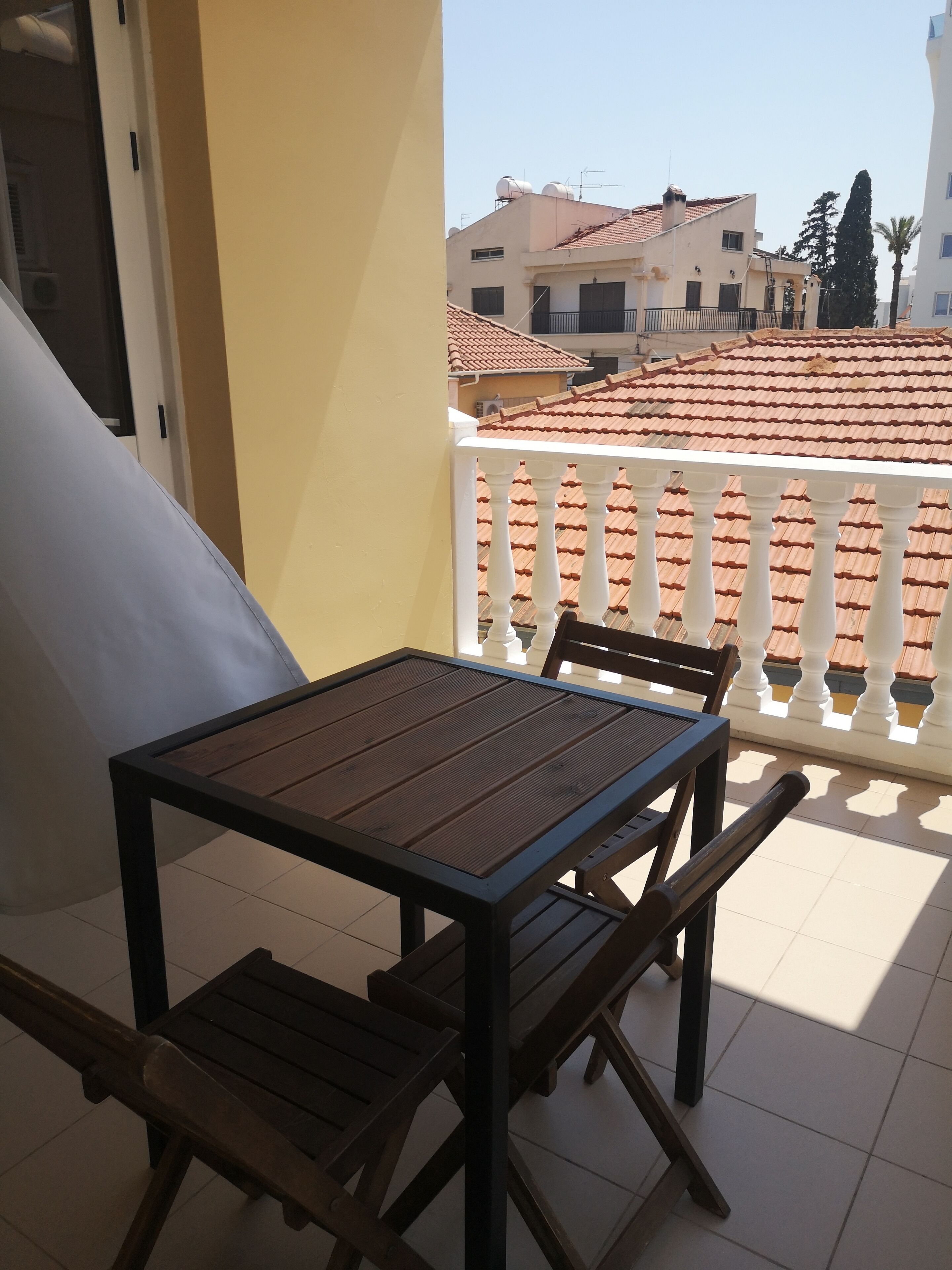A balcony with a table and chairs, overlooking a residential area with tiled roofs and white railings.