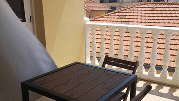 A balcony with a table and chairs, overlooking a residential area with tiled roofs and white railings.