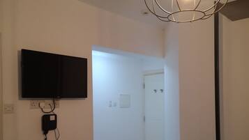 Un pasillo con un televisor de pantalla plana montado en la pared, un teléfono y una lámpara moderna.