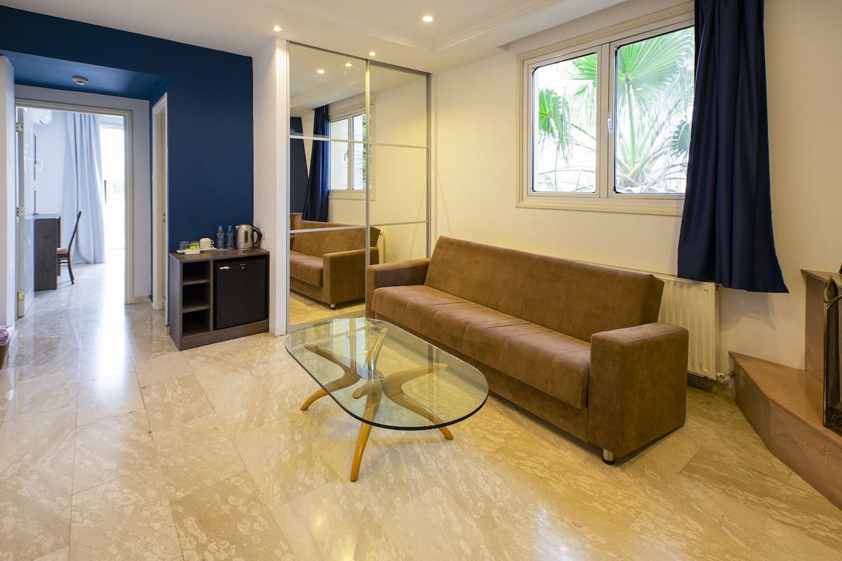 Una sala de estar moderna con una mesa de centro de vidrio, un sofá marrón y vistas a una cocina y comedor a través de una puerta abierta.