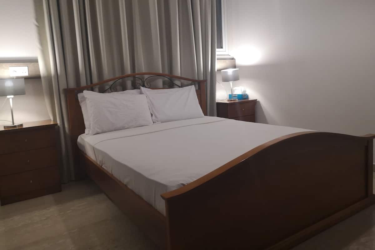 Una cama bien hecha con sábanas blancas, un cabecero de madera y dos mesitas de noche con lámparas.