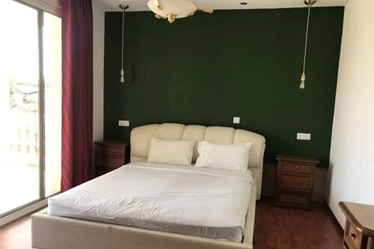 Un dormitorio con una cama, dos mesitas de noche, una lámpara en el techo y una ventana con cortinas.