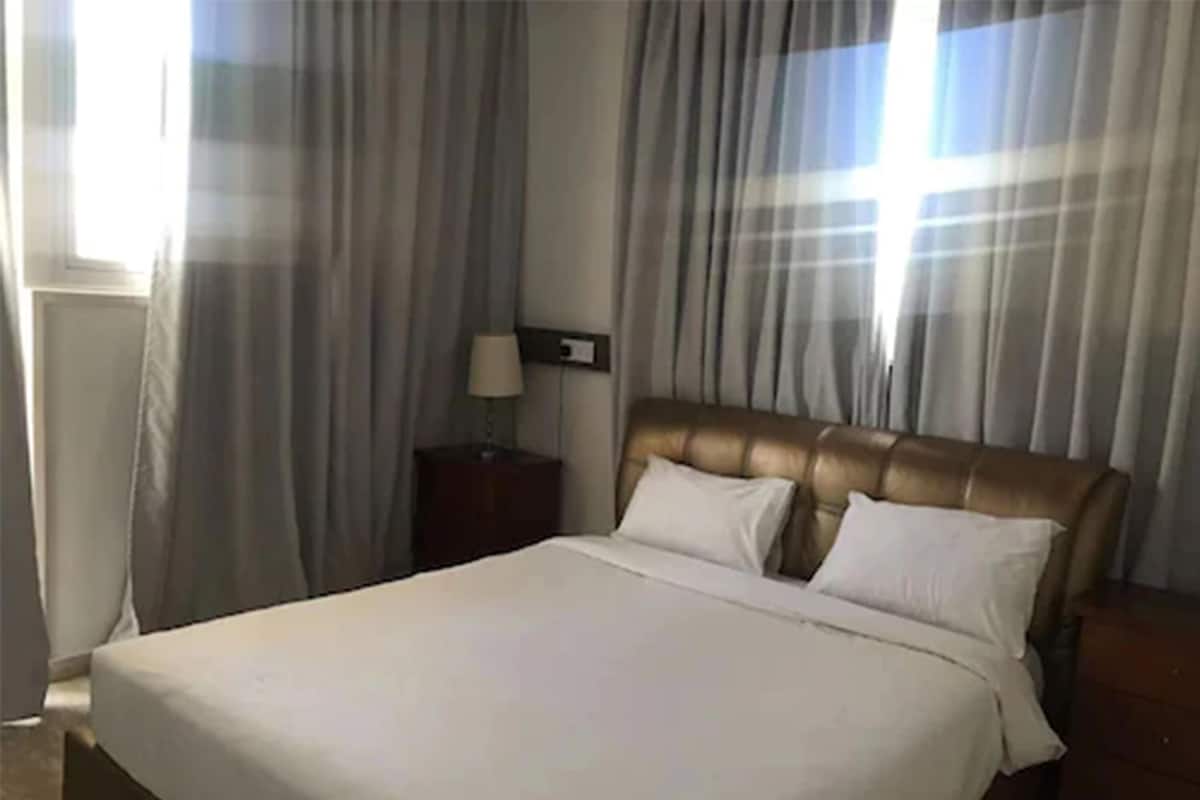 Una habitación de hotel con una cama grande, una mesita de noche con lámpara y una ventana con cortinas.