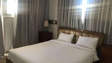 Une chambre d’hôtel avec un grand lit, une table de chevet avec une lampe et une fenêtre avec des rideaux.