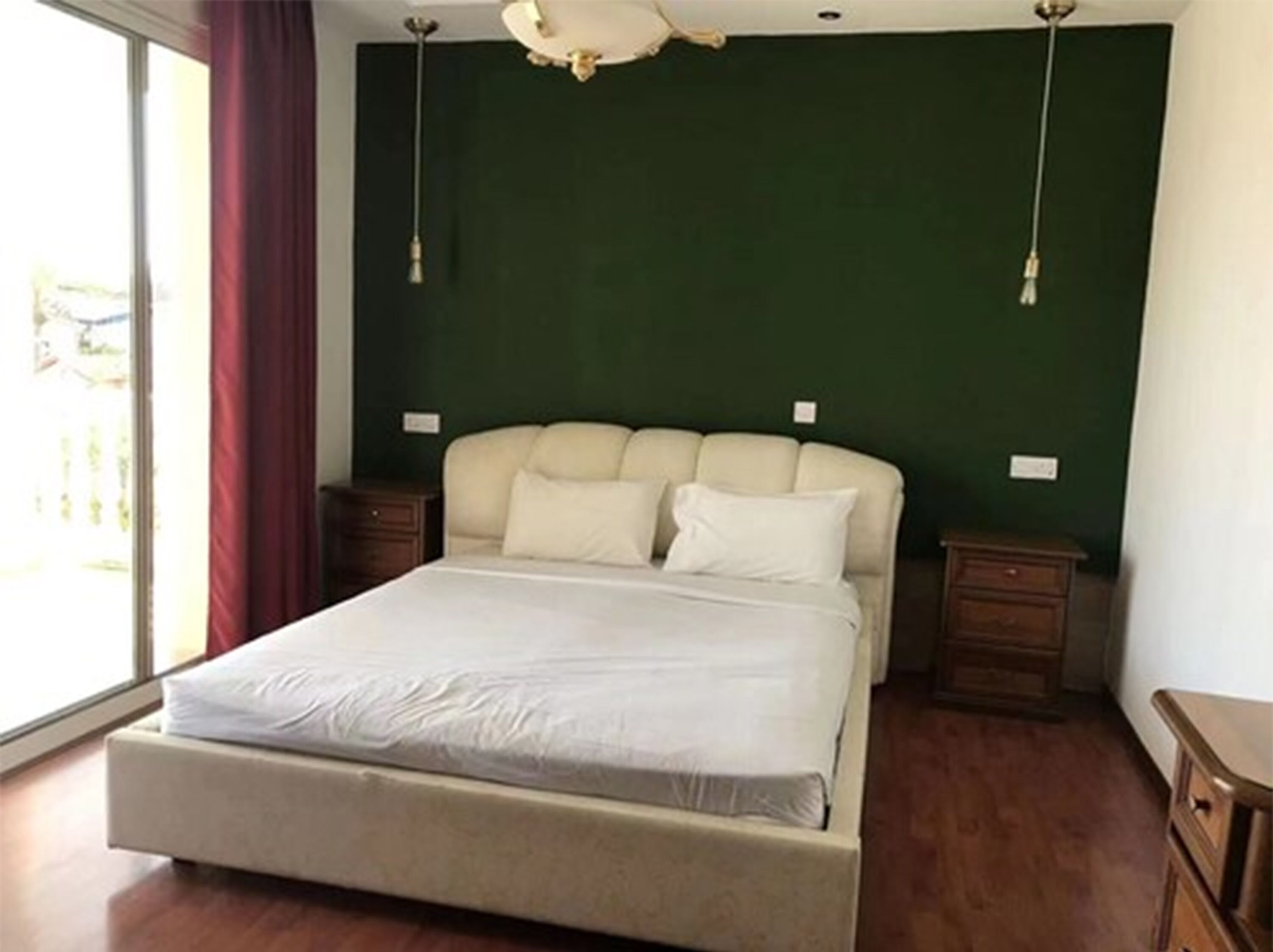 Un dormitorio con una cama, dos mesitas de noche, una lámpara de techo y una ventana con cortinas.