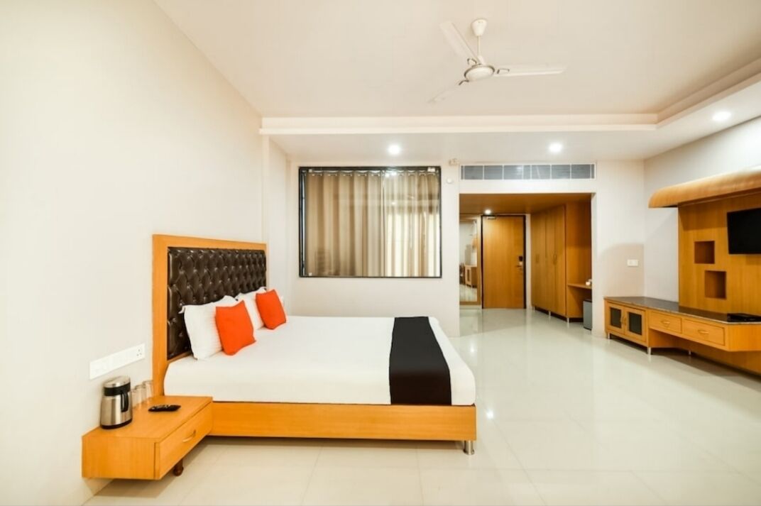 A modern hotel room with a large bed, a TV, a wooden cabinet, and a ceiling fan.