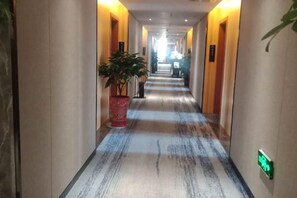 A hotel corridor with a carpeted floor, potted plants, and doors leading to rooms. - Kaisheng Hotel (Xiangtan)