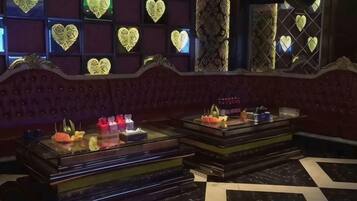 A room with a dark red upholstered sofa, a glass display case with items, and a patterned wall with heart-shaped designs.