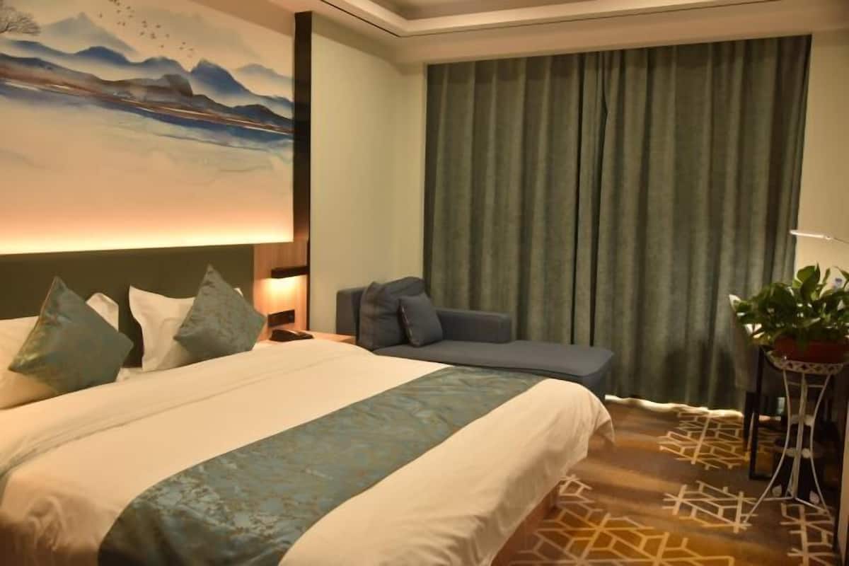 A hotel room with a bed, a sofa, a nightstand, a lamp, a curtain, and a plant.