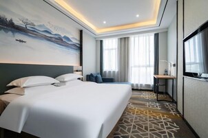 Una habitación de hotel con una cama grande, un escritorio, una silla, un televisor y un cuadro en la pared.