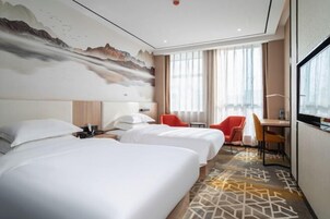 Habitación de hotel con dos camas, un escritorio, una silla y un ventanal grande.