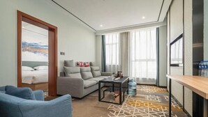 Une chambre d’hôtel moderne équipée d’un canapé, d’une table basse, d’une télévision et d’une grande fenêtre avec des rideaux.