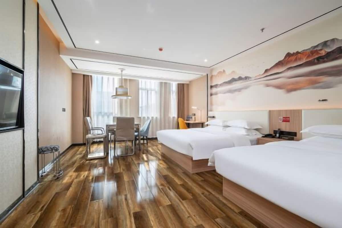 A hotel room with two beds, a desk, a chair, and a large window.
