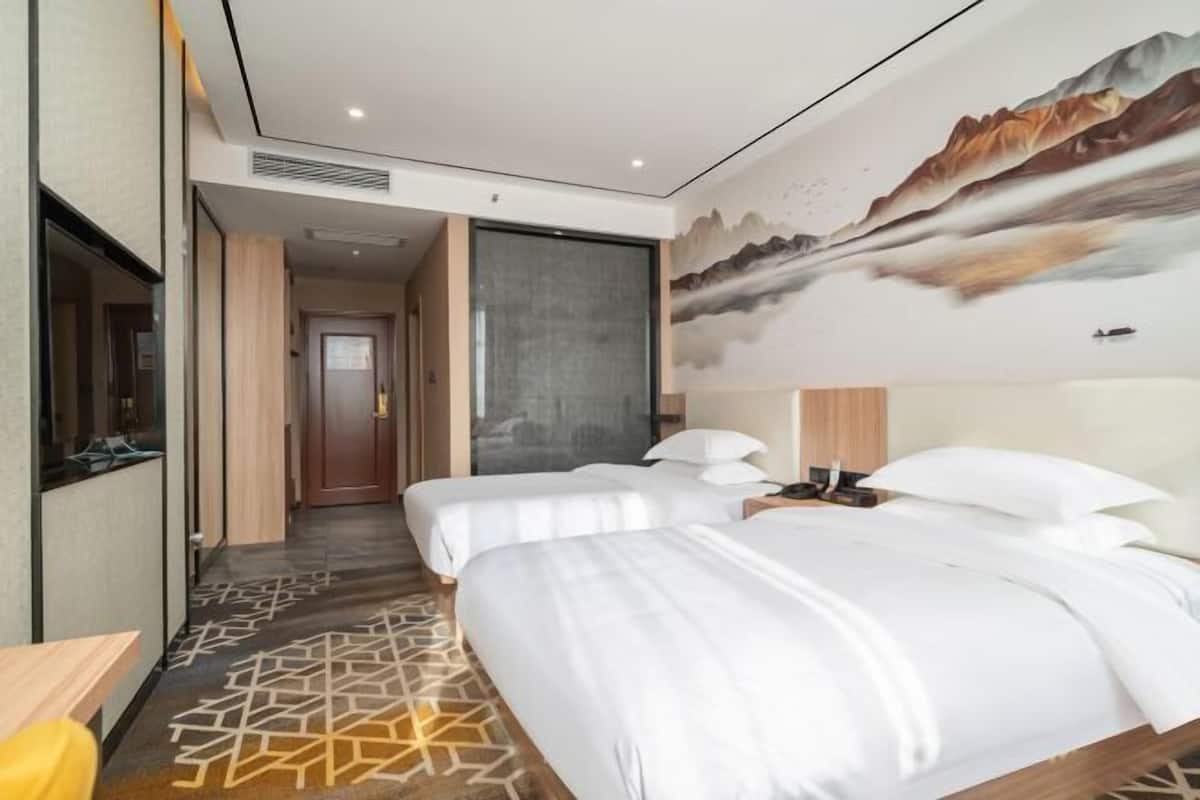 A hotel room with two beds, a large painting on the wall, and a patterned carpet.