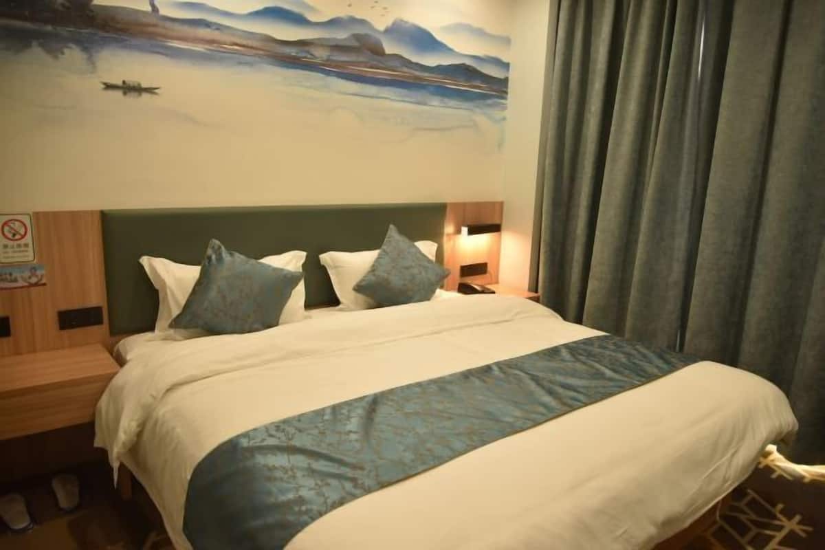 A hotel room with a bed, pillows, a nightstand, a wall painting, and a curtain.