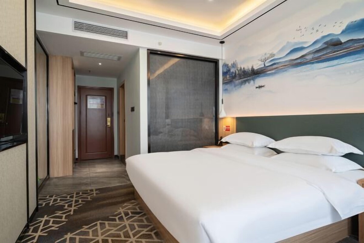 A hotel room with a large bed, a painting on the wall, and a door leading to another room.