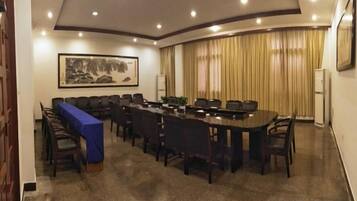 Un salón de conferencias con una mesa larga, sillas, un mantel azul y una obra de arte enmarcada en la pared.