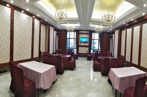 A banquet hall with multiple round tables and chairs, a chandelier, and a television screen on the wall.