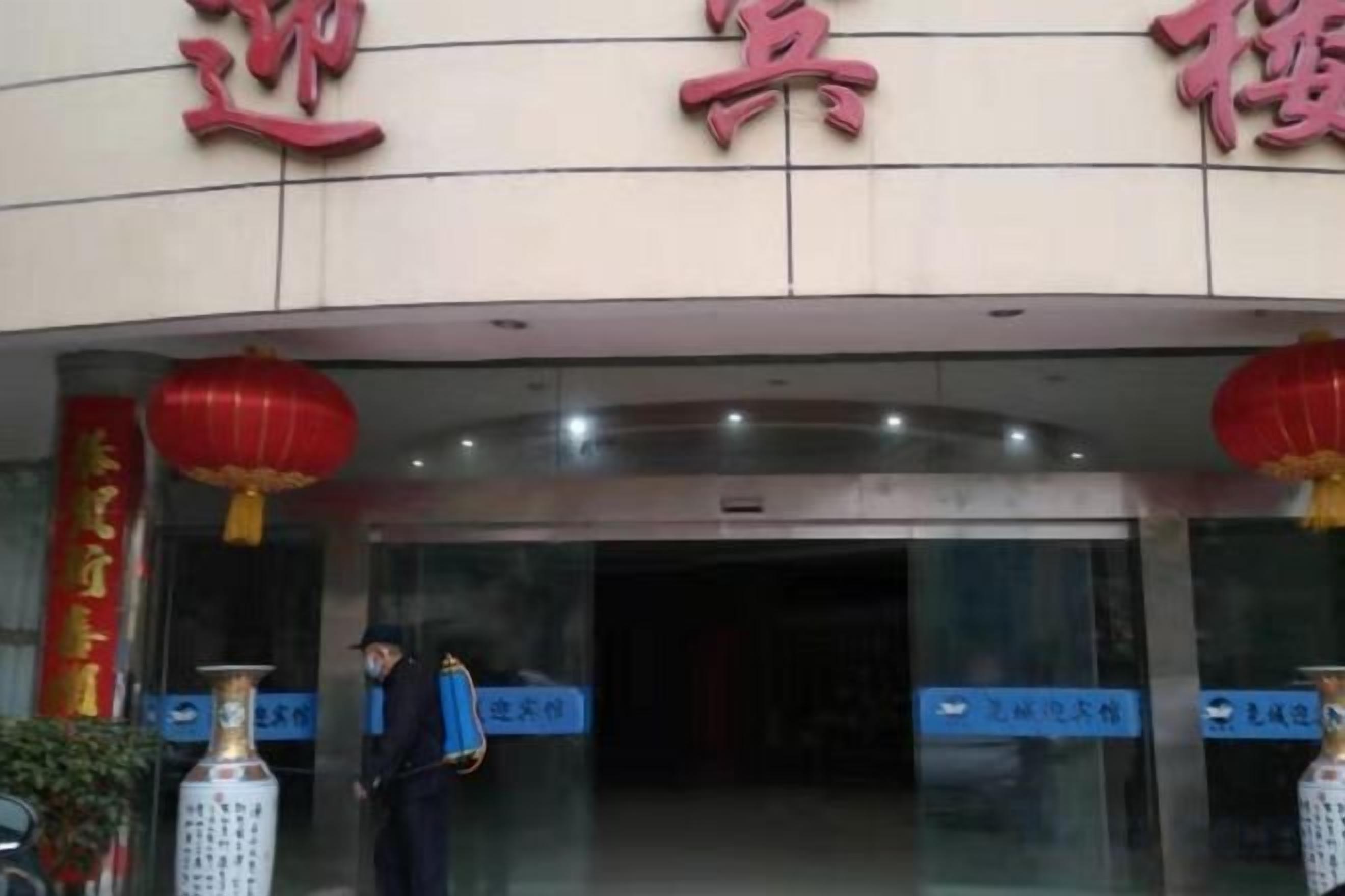 A hotel entrance with a sign above the door, a person standing in front, and a red lantern hanging above.