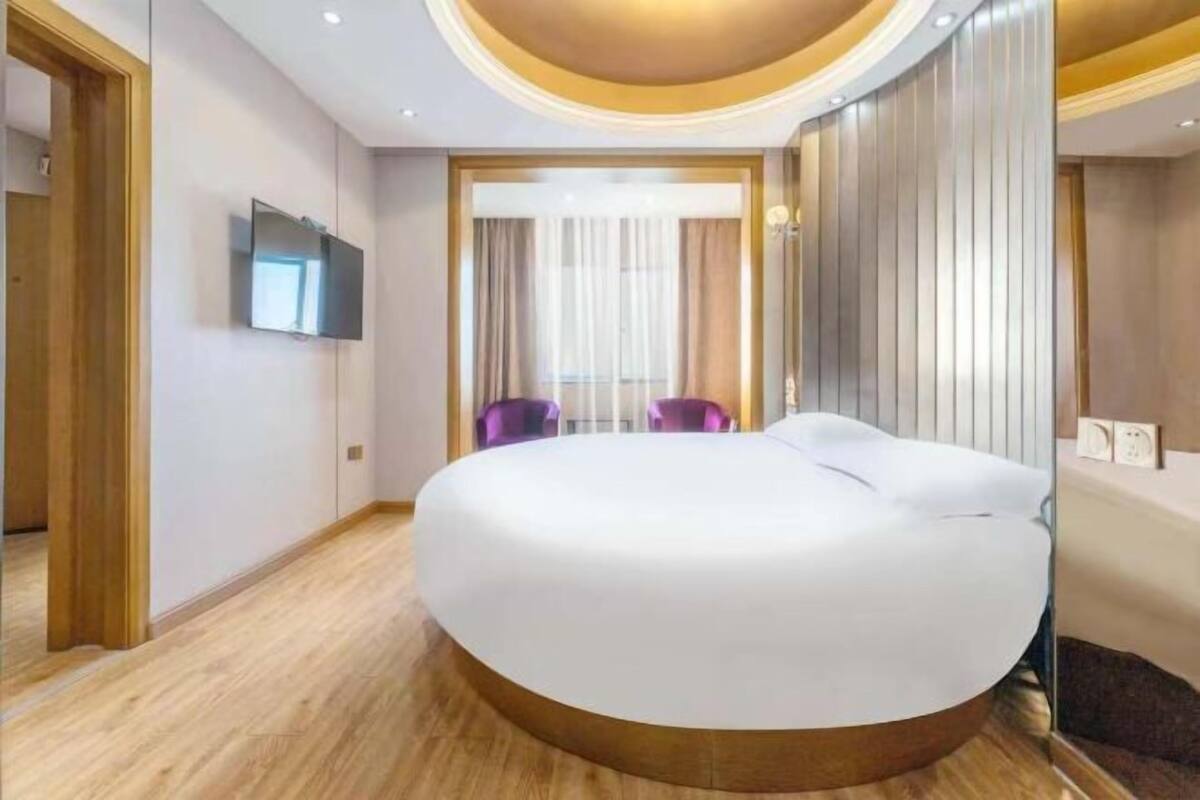 Ein modernes Hotelzimmer mit einem großen, runden Bett, einem an der Wand befestigten Fernseher und einem Holzboden.