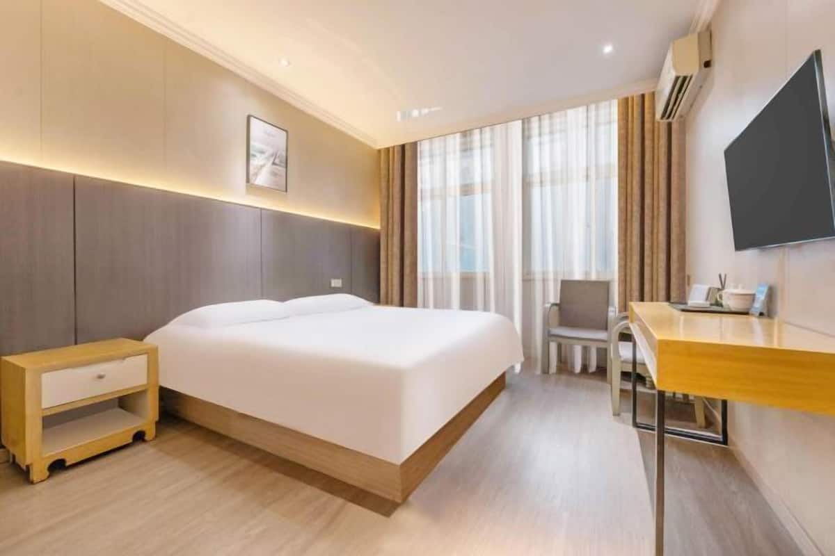 Ein Hotelzimmer mit Bett, Nachttisch, Stuhl, Schreibtisch und einem an der Wand befestigten Fernseher.
