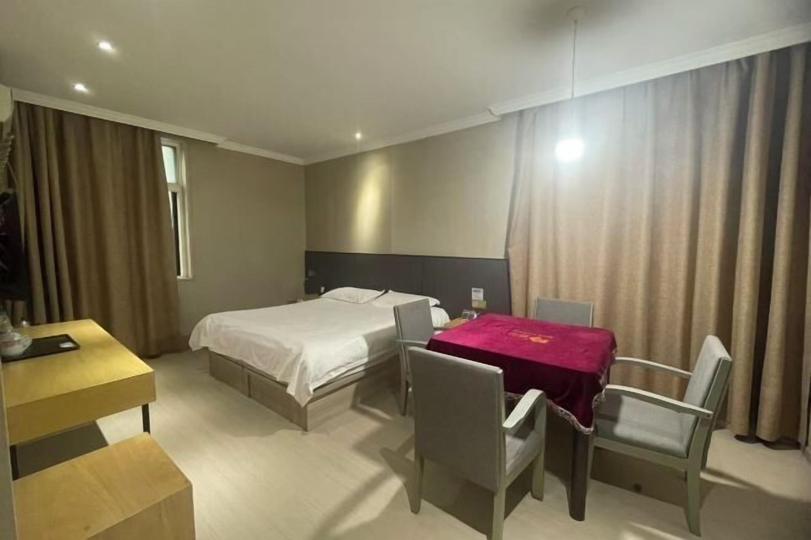 Une chambre d’hôtel avec un lit, un bureau, une chaise et une table recouverte d’une nappe rouge.