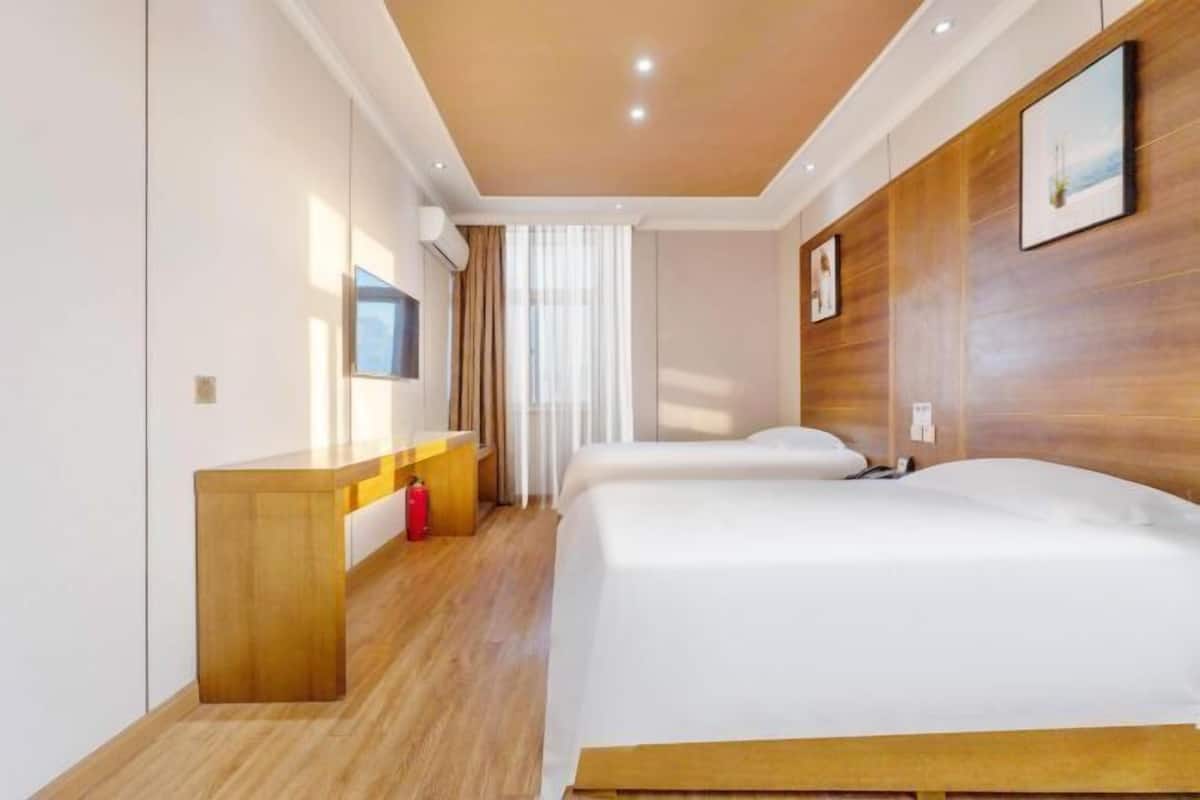Ein Hotelzimmer mit Holzboden, einem Bett mit weißer Bettwäsche, einem Holz-Kopfteil, einem Nachttisch, einem Spiegel und einem Fenster mit Vorhängen.